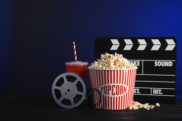 Composition with popcorn, cinema clapperboard and film reel on table against color background....