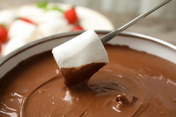 Dipping marshmallow into pot with tasty chocolate fondue, closeup