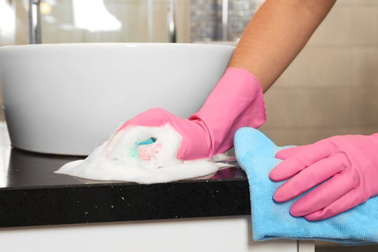 Woman in protective gloves cleaning bathroom countertop with sponge, closeup