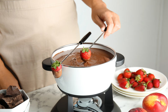Woman dipping strawberry into pot with chocolate fondue on table, closeup