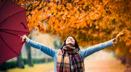 Young beautiful brunette girl in blue coat with umbrella walking in the autumn park