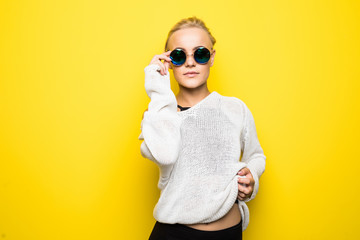Portrait of smiling beautiful blonde girl in sunglasses against yellow background