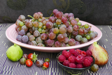 A pink platter of purple grapes with figs and berries