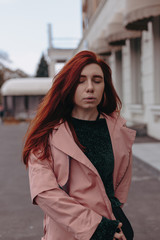 Obraz premium Beautiful and stylish girl with red hair walks in the city and her hair is in the wind