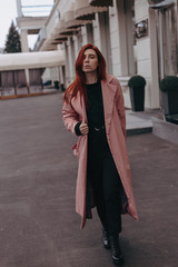 Naklejka premium Beautiful and stylish girl with red hair walks in the city and her hair is in the wind