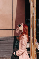 Fototapeta premium Beautiful and stylish girl with red hair walks in the city and her hair is in the wind