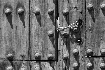 Chain lock on old wooden door with round rivets. Gate closed, no entry, no trespassing, vintage concepts. Black and white photography
