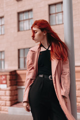Obraz premium Beautiful and stylish girl with red hair walks in the city and her hair is in the wind