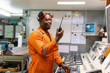 African marine engineer officer in engine control room ECR. He speaks with VHF or UHF portable...