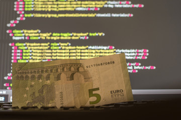Money on the keyboard and computer display with code on the background