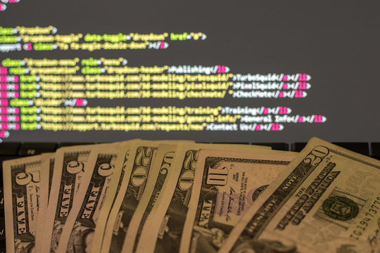 Money on the keyboard and computer display with code on the background