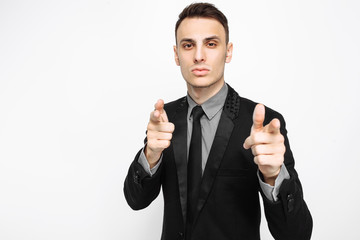 handsome young man in black suit, fun, smiling, pointing fingers at camera, trying to get your attention, on white background