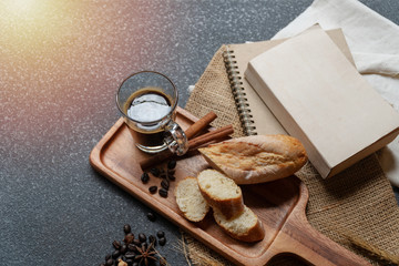 Cup of black coffee with bread on wood plate with book, dry flower on table.
