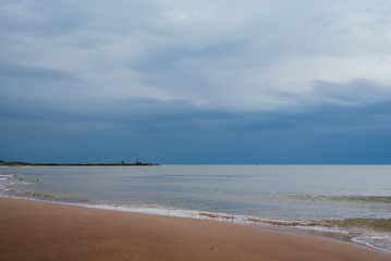 White sand beach with waves and blue sky on cold summer day in Latvia, Pavilosta, port with lighthouse in the background