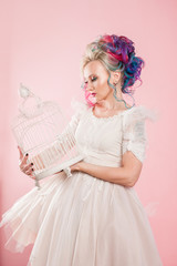 Stylish girl in white dress. Creative hair coloring. Multi-colored hairstyle. Concept with an empty bird cage.