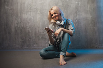 Young and attractive woman with smartphone and large headphones, sitting on the floor. Music in the...