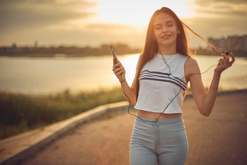 Young beautiful caucasian girl listening to music with smartphone walking in the city with...