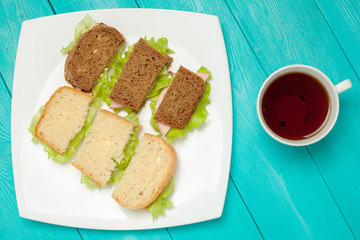 Bruschetta of white and black bread lay on a plate. The dish of sandwiches standing on the wooden surface. A Cup of coffee next to a plate of sandwiches. Flat lay of food on a table.