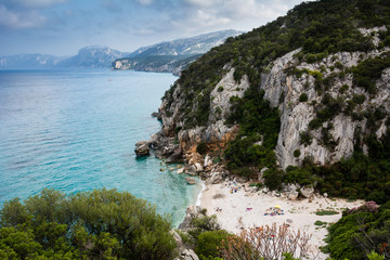 Cala Gonone beach in Sardinia with unrecognizable people on an overcast summer day, perfect vacation place. Seascape view.