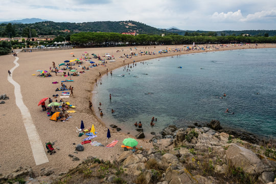 Turquoise beach of Torre di Bari, Sardinia, Italy with unrecognizable people sunbathing. Beautiful blue sky with clouds and mountains in the background and a path visible.