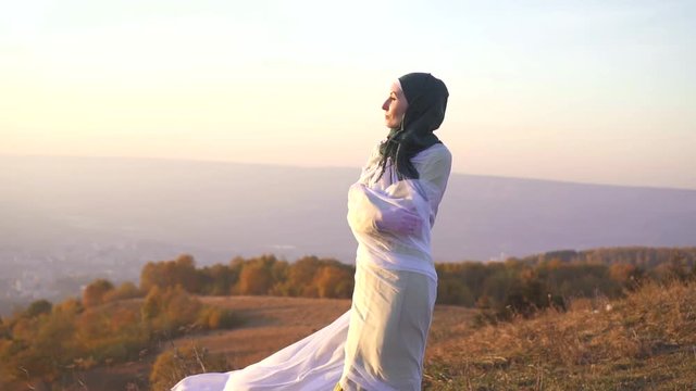 portrait of a stylish girl in a hijab at sunset in the mountains stands on the edge of a cliff