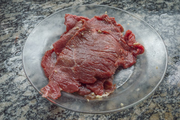 meat, raw beef steak being seasoned in a transparent dish, on top of marble table