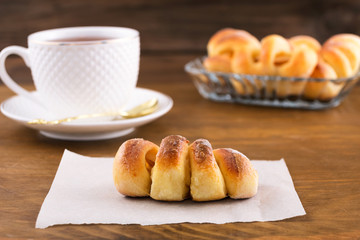Sweet dessert-pastries with fruit filling and tea in a white mug, wooden background.
