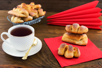 Homemade curly pastry stuffed with pear slices on a red napkin, tea in a white mug, wooden background.