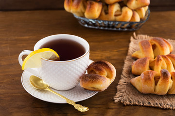 Pastries with fruit filling, tea with a slice of lemon in a white mug, wooden background.