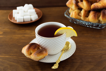 Delicious Breakfast of pastries with tea in a white mug, a slice of lemon, wooden background.