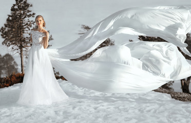Fototapeta na wymiar pretty young woman posing in wedding dress with train, on winter snow