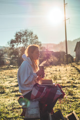 girl sits on a wooden bench in the mountains in nature, reads a book, drinks hot tea from a thermo cup. Concepts Reading in nature