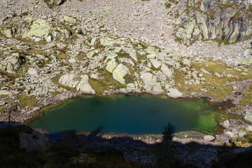 Autumn hiking in Aosta valley, Gressoney, Italy. View of alpine lake of Goudin descendig from  Sella pass. The path is alredy in the shade.