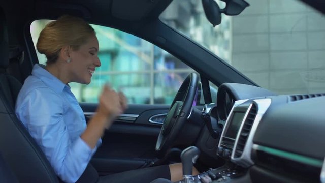 Woman delighted with first purchased car, touches random buttons, naive joy