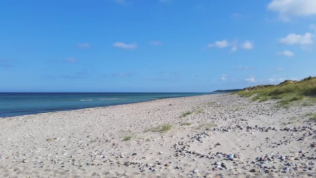 Liseleje Beach by the Tisvilde forest and coastal area on the Danish island of Zealand.  
A pristine spring morning with a sunny blue sky. Gentle ocean waves and scattered beautiful beach stones.