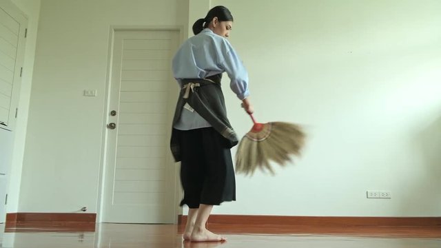 Woman cleaning house with broom stick. Beautiful Asian woman cleaning floor with broom stick, singing along the way. Low angle shot. House cleaning service concept.