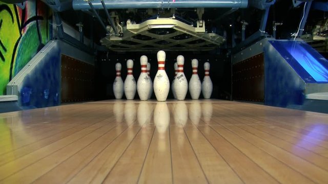 A beautiful shot shows a pinsetter resetting bowling pins for the next shot in a bowling alley with green light on the sweep bar