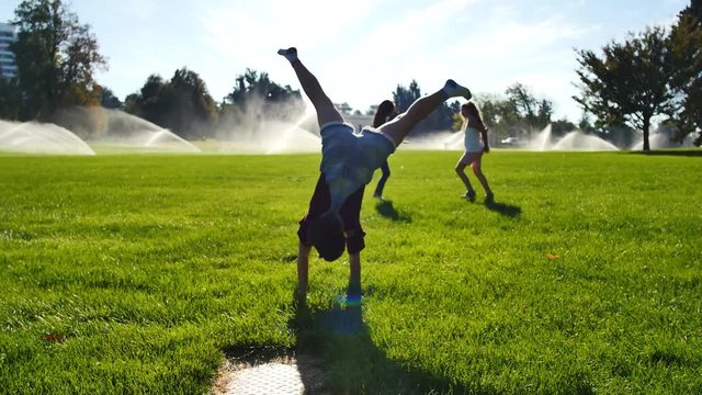 Girls tumbling and doing cartwheels in park by sprinklers