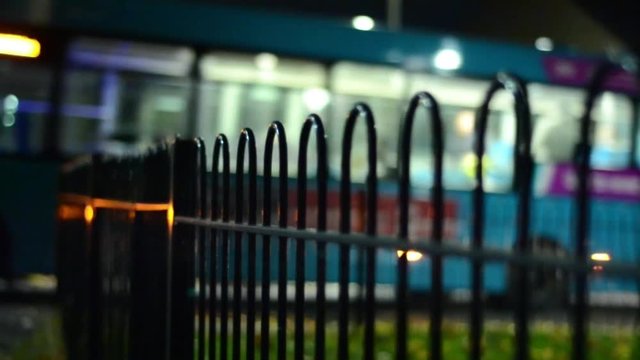 Nighttime view of bus as it passes by from garden railings