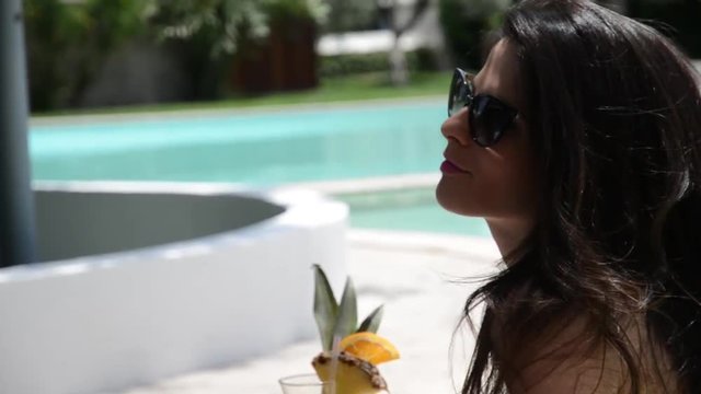 ragazza in bikini sorseggia un drink sul bordo di una piscina