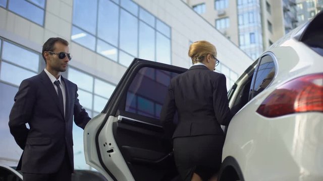 Personal driver meeting and opening car door for lady boss, bodyguard duties