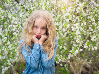 A beautiful girl supports her face with her hands in the spring cherry orchard.