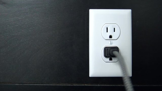Male hand plugs in and unplugs a two pronged cord into the bottom outlet of an American electrical socket Copy Space Left