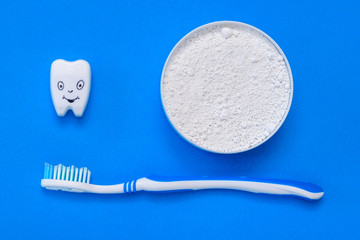 The tooth figurine smiles next to the tooth powder and toothbrush. The view from the top. Flat lay.