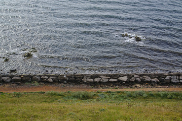 Side of beach with large stones and green grass