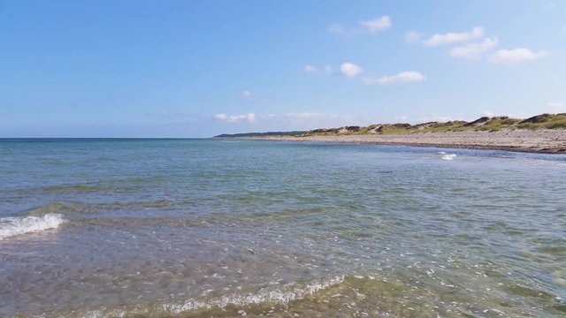 Liseleje Beach by the Tisvilde forest and coastal area on the Danish island of Zealand. A pristine spring morning with a sunny clear blue sky. Shallow water ripples and gentle waves.
