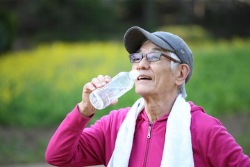 屋外で運動の合間にペットボトルの水を飲む高齢者の男性