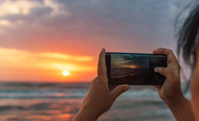 Girl takes pictures on smartphone dawn on the sea