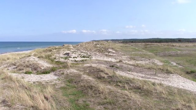 Liseleje Beach by Tisvilde forest and coastal area on the Danish island of Zealand. Overlooking the ocean and sand dunes. On the path behind the dunes are two people out for a walk. Sunny blue sky.