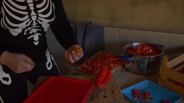 Young female cook in skeleton costume and apron cuts red tomatoes for making tomato sauce. Hands close up.